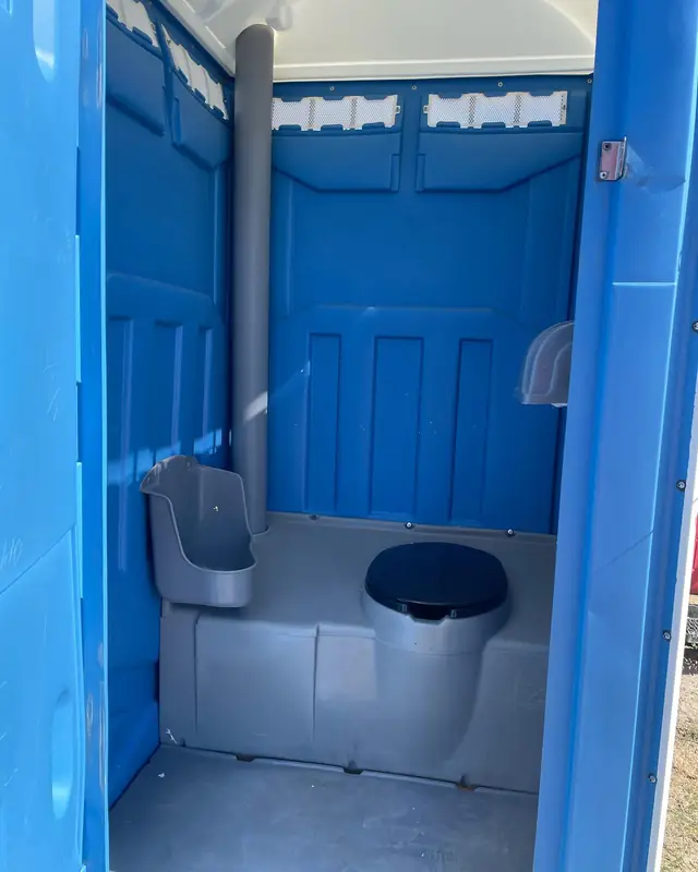 Inside a blue standard porta potty showing the urinal, toilet seat and toilet paper holder