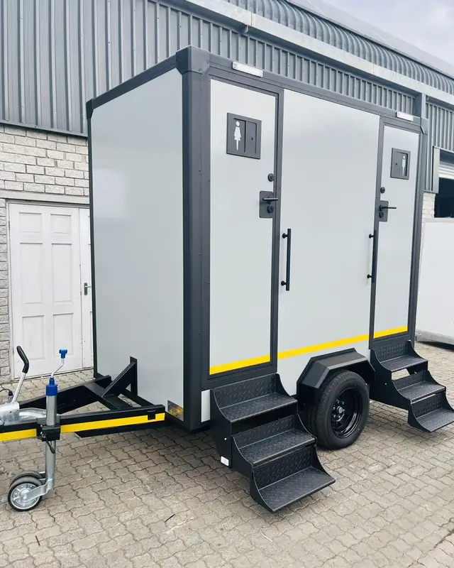Gray two-stall restroom trailer with separate doors and folding steps